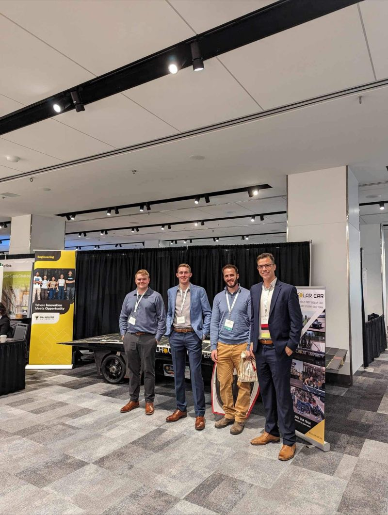 Four attendees beside a Dalhousie University solar car exhibit.