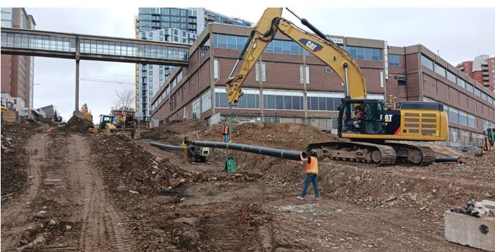Workers and an excavator installing underground piping at the Cogswell district energy construction site.