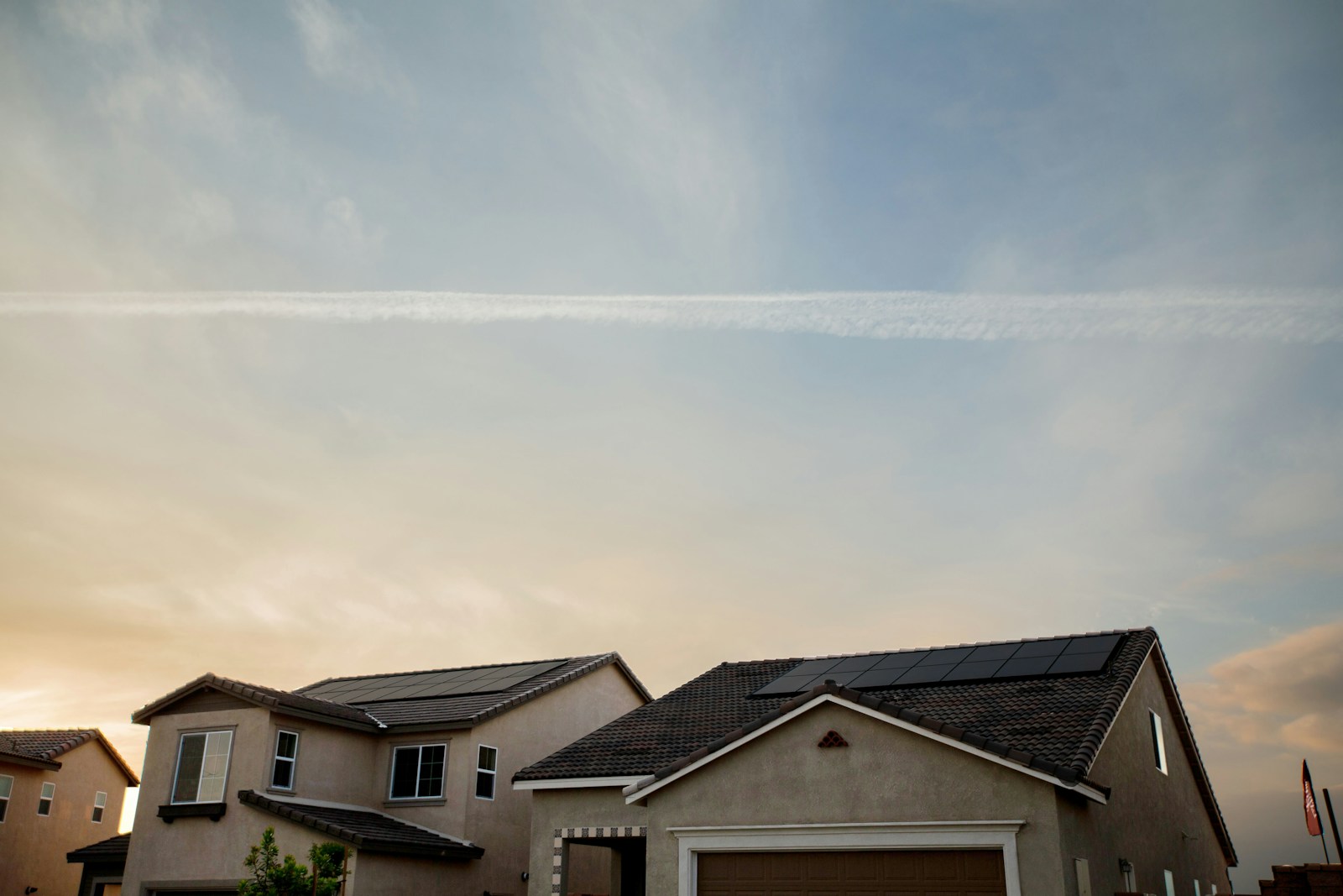 Rooftop solar panels on two neighbouring homes beneath an evening sky.
