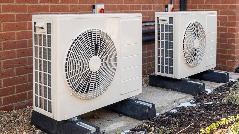 Two outdoor heat pump units mounted beside a brick wall.